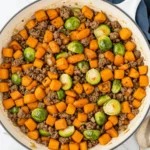 Ground beef and sweet potatoes skillet with Brussels sprouts and carrots in white enamel pan