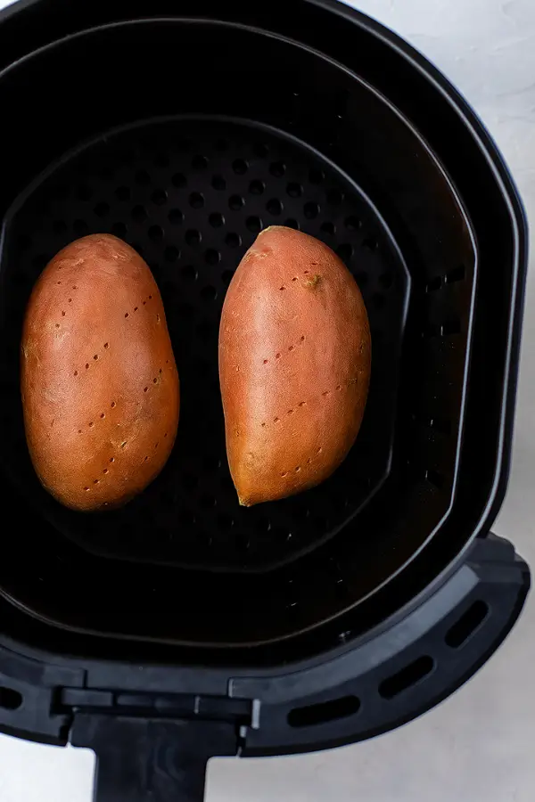 Two sweet potatoes cooking in air fryer basket
