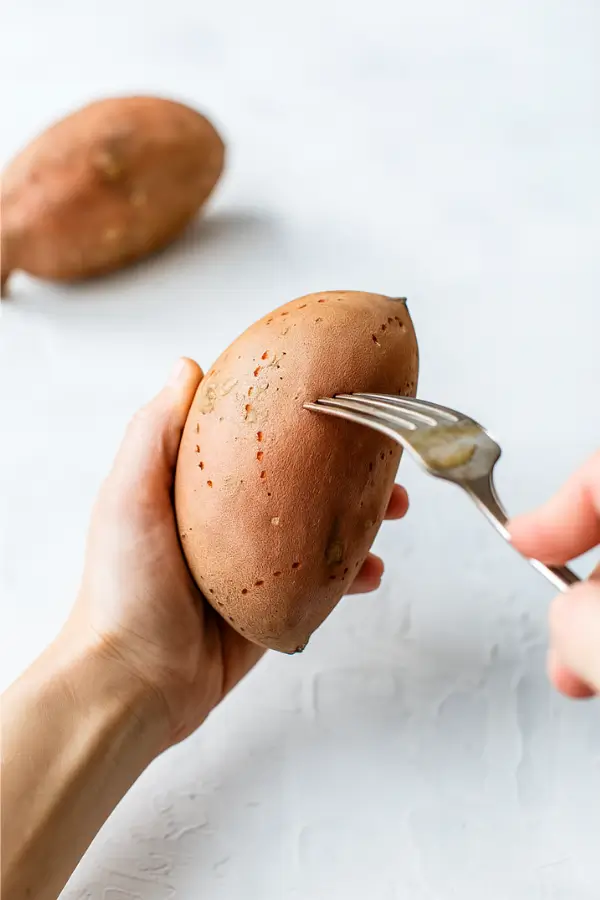 Hand piercing sweet potato with fork before air frying