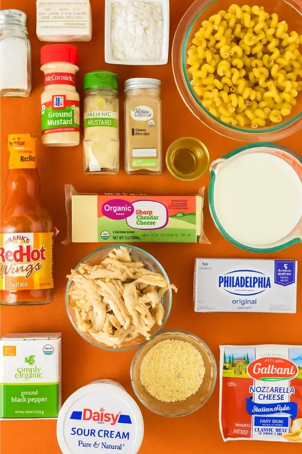Flat lay of ingredients for buffalo chicken mac and cheese on an orange background.