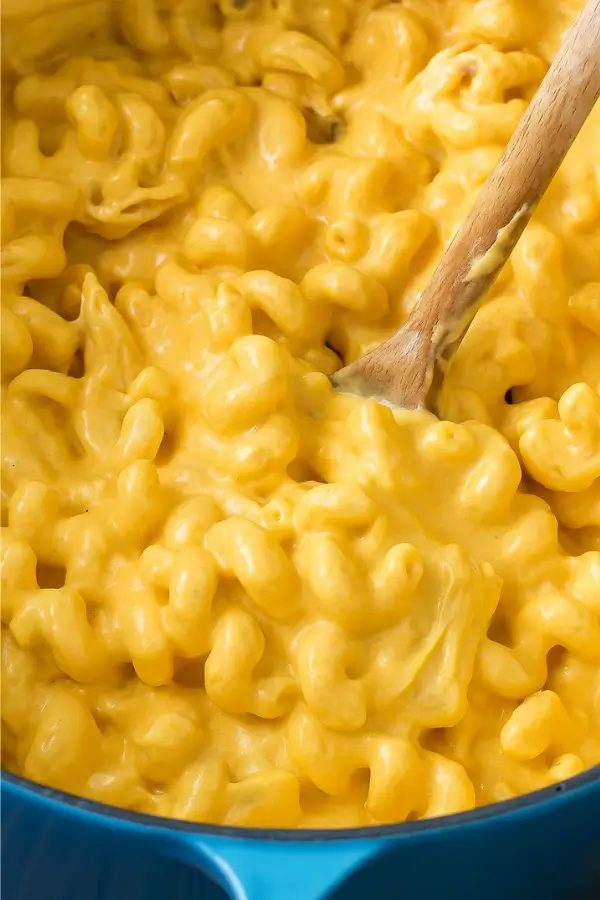 Buffalo chicken mac and cheese being stirred in a blue pot with a wooden spoon.