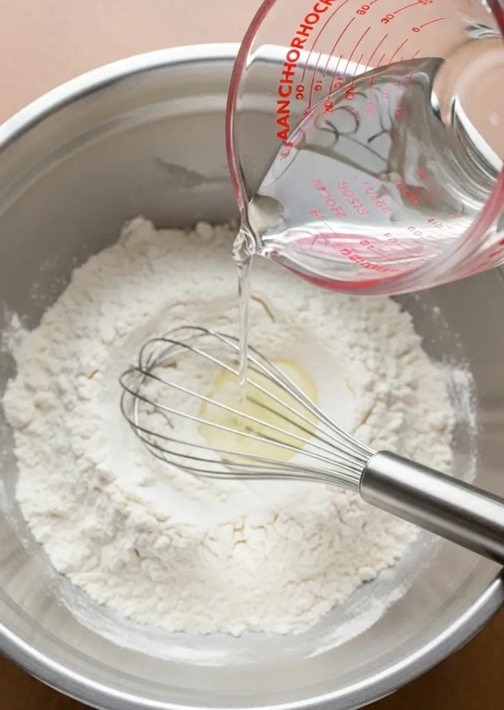 Pouring water into flour mixture to make kataifi pastry batter