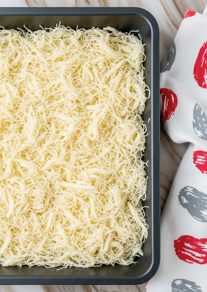 Unbaked kataifi pastry strands in a metal baking tray