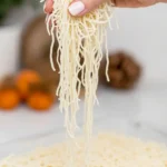 Hand lifting uncooked kataifi pastry strands from glass dish