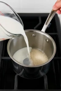 Pouring whole milk into a saucepan with sugar to start the ice cream base