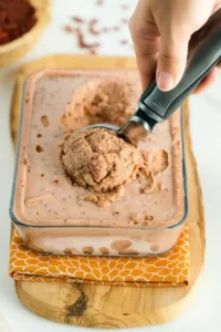 Hand scooping frozen red bean ice cream from a glass container