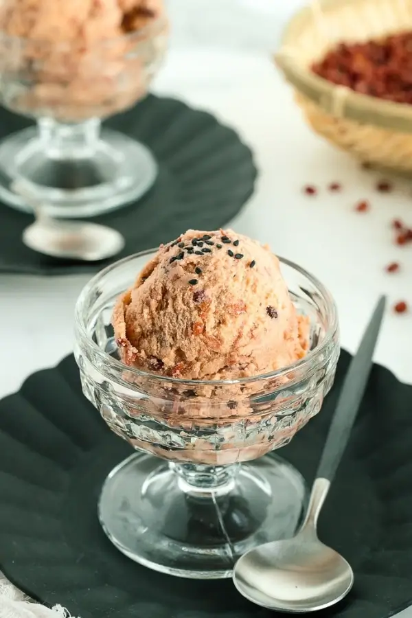 A scoop of red bean ice cream in a glass bowl topped with black sesame seeds