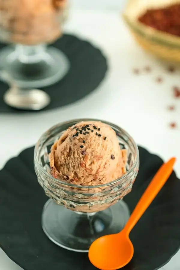 scoop of red bean ice cream in a glass bowl with black sesame seeds and an orange spoon