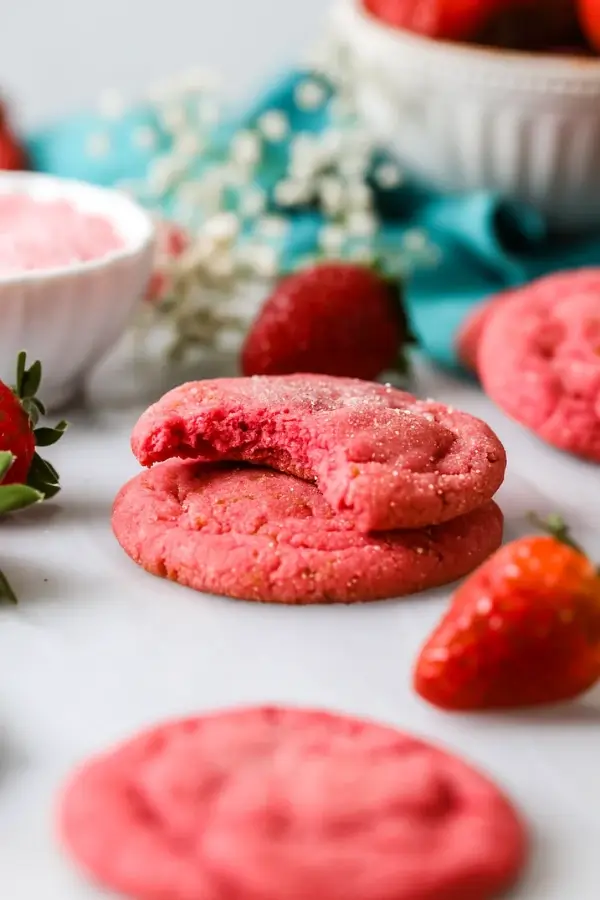 Strawberry sugar cookie with a bite taken out, stacked on another cookie.