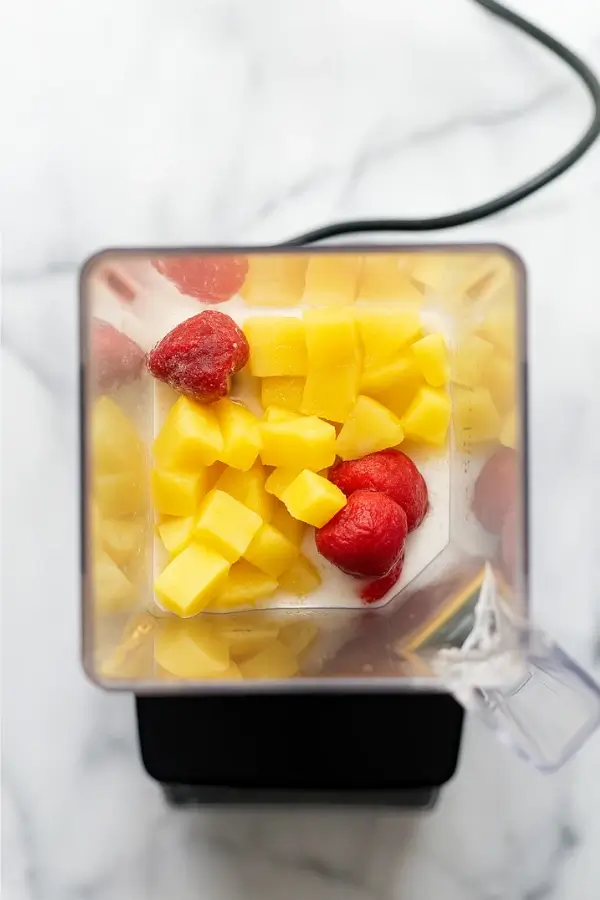 blender with frozen strawberries and pineapple chunks