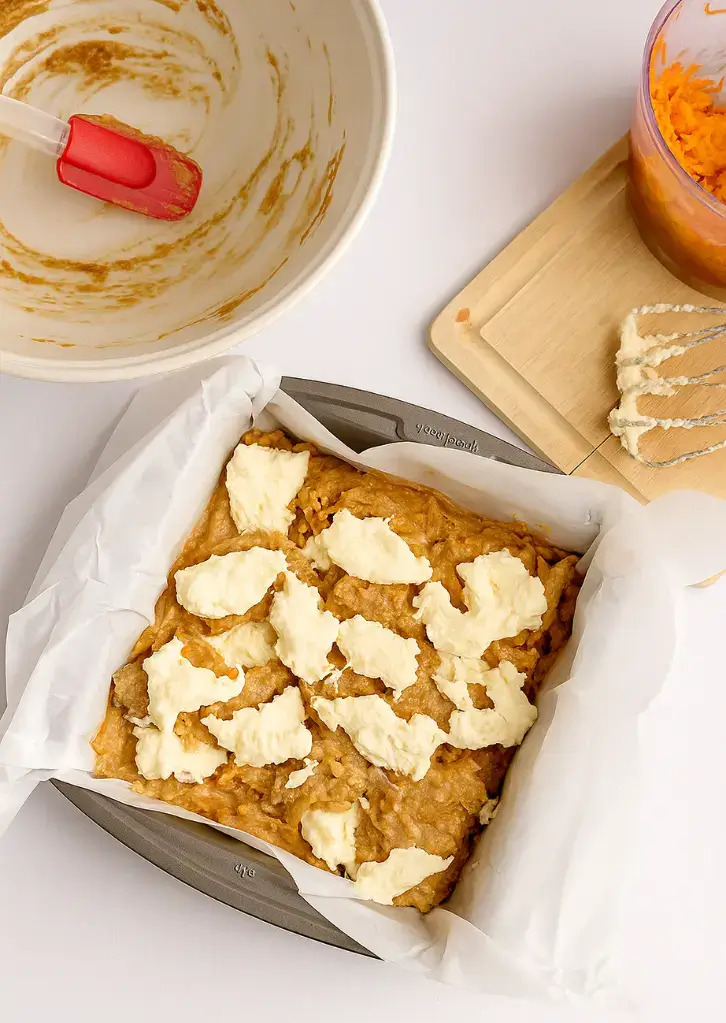 Cheesecake dollops over carrot batter in baking pan