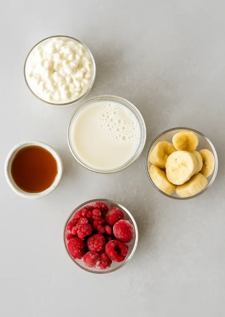 Smoothie ingredients including cottage cheese, banana, raspberries, milk, and honey