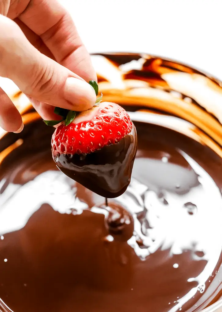 hand dipping strawberry into melted dark chocolate