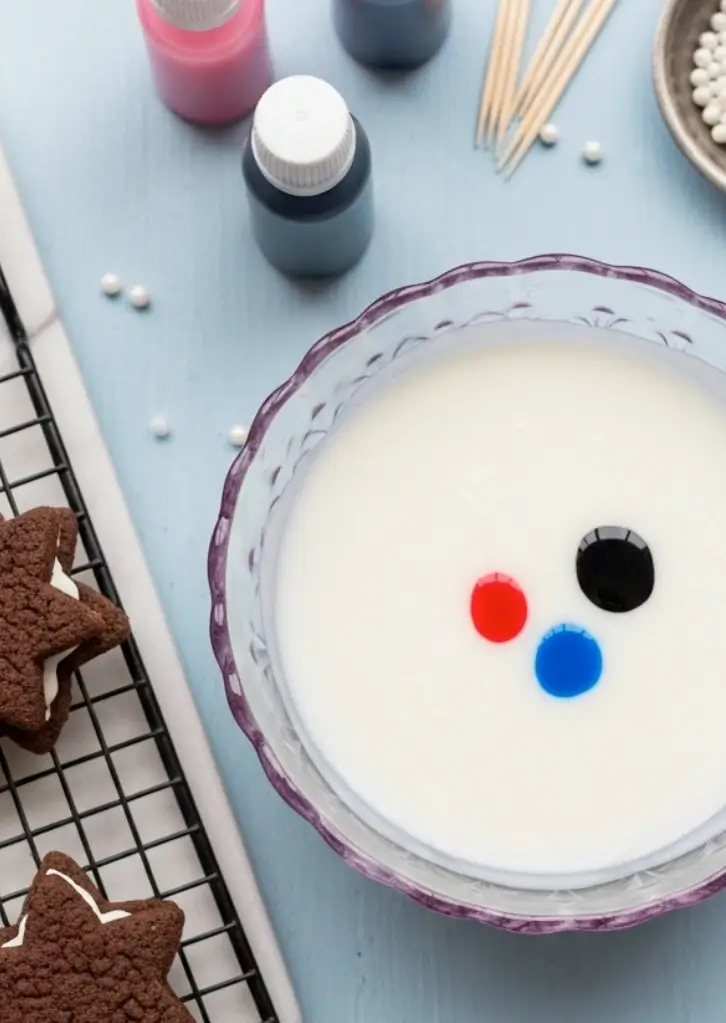 Bowl of icing with gel food coloring drops and decorating tools