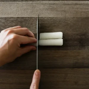Slicing cylinder rice cake with knife on wood board