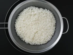 Drained soaked rice in a metal strainer for garaetteok