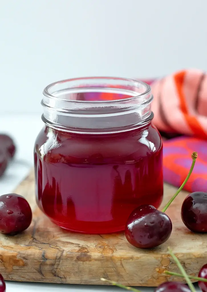 jar of homemade cherry syrup with fresh cherries