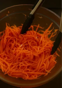 Julienne carrots in a bowl with tongs