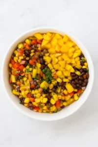 Half-mixed mango black bean salad in a white bowl on a white background