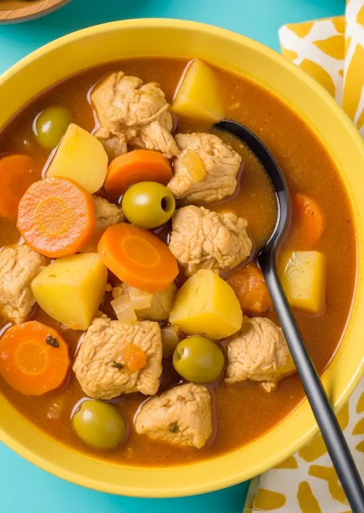 Served bowl of Pollo Guisado with chicken, potatoes, carrots, and olives