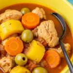 Close-up of Pollo Guisado with tender chicken, carrots, potatoes, and green olives