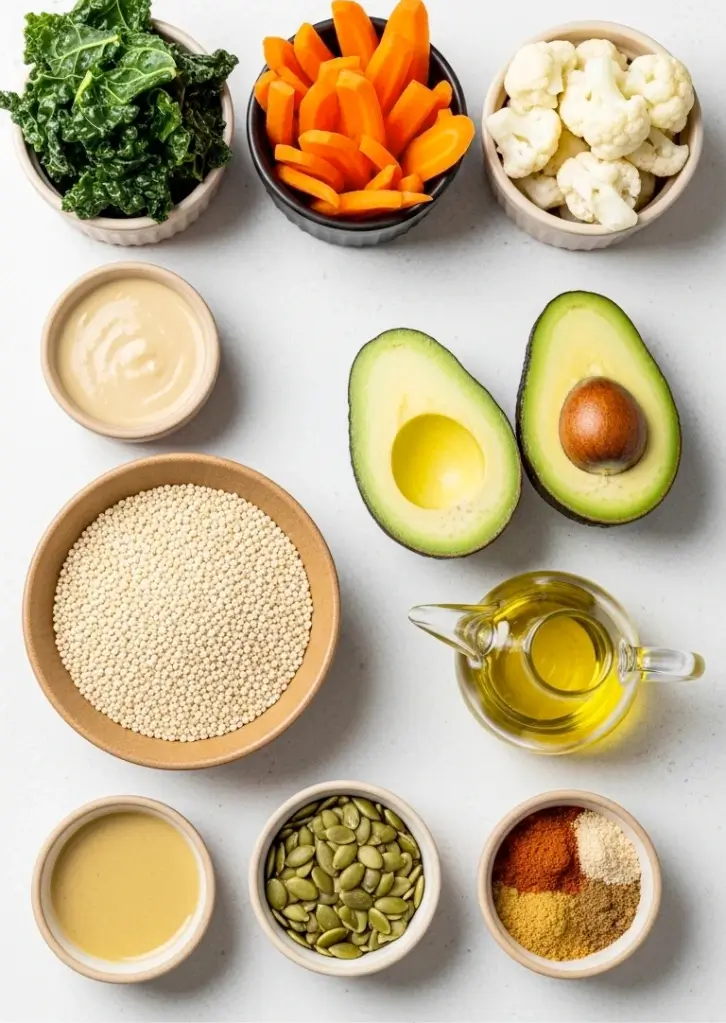 roasted veggie bowl ingredients laid out in bowls including kale, carrots, cauliflower, avocado, quinoa, tahini, olive oil, and spices