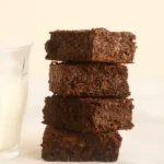 Close-up of moist sweet potato brownies stacked beside milk