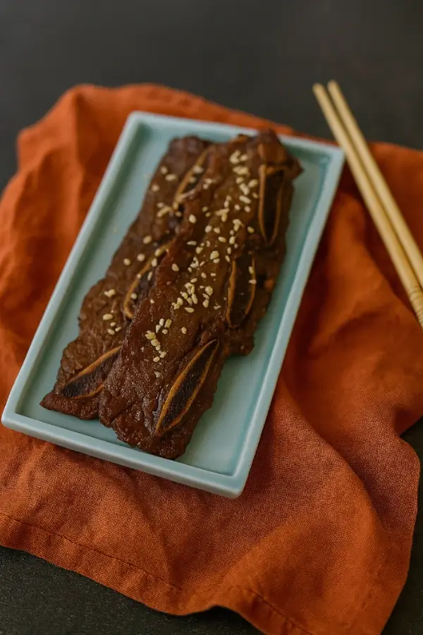 Plated LA Galbi ribs with sesame seeds on a blue tray beside chopsticks