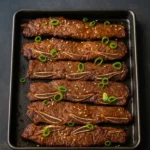 Sheet pan of grilled LA Galbi ribs topped with sesame seeds and scallions