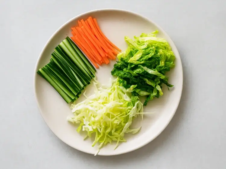 Plate of julienned cucumber, carrots, shredded cabbage, and lettuce