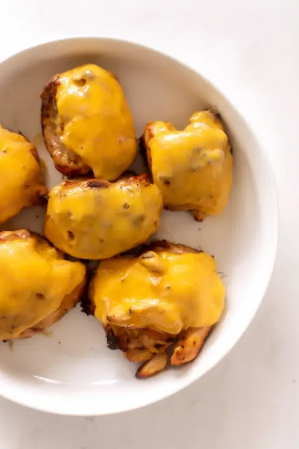 Chicken pieces topped with melted cheddar cheese on a white plate