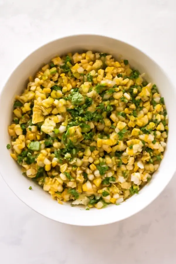 A bowl filled with a corn salad featuring corn kernels, green onions, and fresh herbs