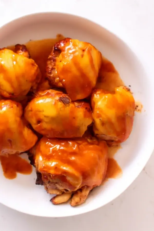 Cheddar-topped chicken pieces drizzled with buffalo sauce on a white plate