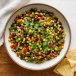 Overhead view of Cowboy Caviar in a ceramic bowl with tortilla chips on the side.
