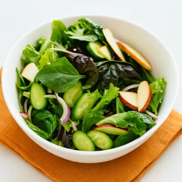 Tossed Korean Green Salad in a white bowl showing evenly coated greens, cucumber, apple, and onion