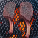 Tomahawk steaks cooking on a grill over open flames